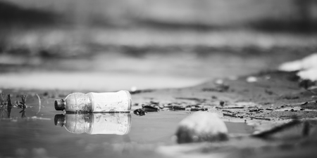 Abandoned empty pink plastic bottle garbage at the river bank conservancy pollution black and white...