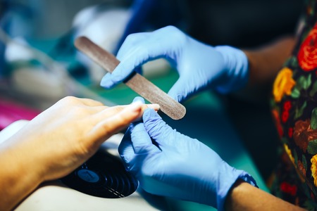 Manicurist master make manicure in blue gloves with nail file. Woman getting nail manicure.の写真素材