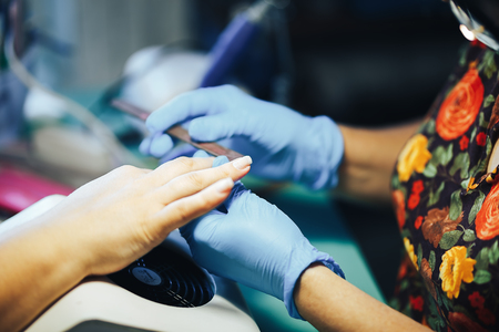 Manicurist master make manicure in blue gloves with nail file. Woman getting nail manicure.の写真素材