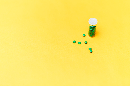 Medical green pills in a glass bottle on yellow background copyspace, health.