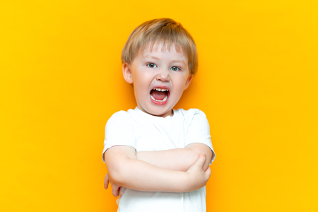 cue little 3 years old boy standing and open hos mouth shout loudly, arms folded on chest, in white t-shirt.の写真素材