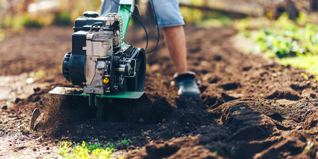close up photo of gardener cultivate ground soil rototiller , tiller tractor, cutivator, miiling machine, prepare for planting crop, spring. modern farming, technology agriculture.の写真素材