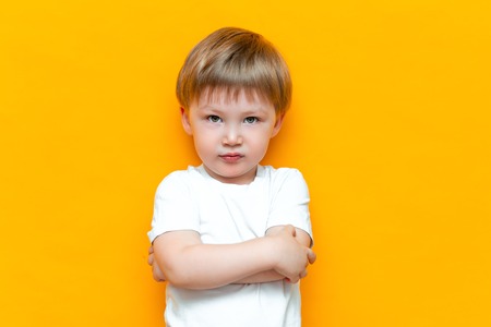 Portrait of angry little boy with arms folded isolated on yellow background. Sad and unhappy child. Upset toddler boy.の写真素材