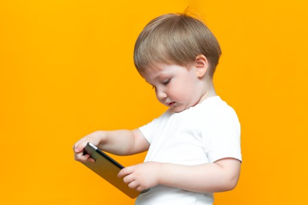 Mixed racial blonde boy using tablet pc on yellow background.の写真素材
