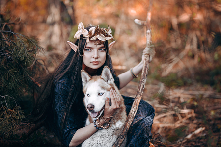 beautiful elf woman fabulous, fairy forest, famtasy young woman with long ears, long dark hair golden wreath crown on head with red dog like wolfの写真素材