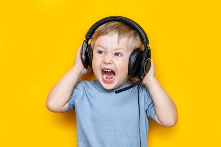 handsome little boy in modern headphones and shouting while standing on yellow background.の写真素材