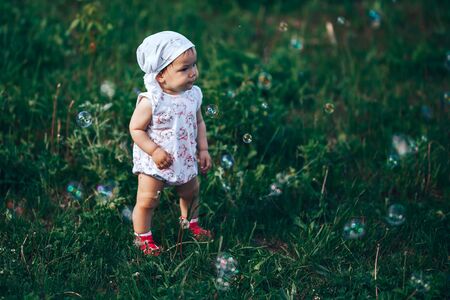 A little girl blowing soap bubbles, spring portrait beautiful one year old kid.