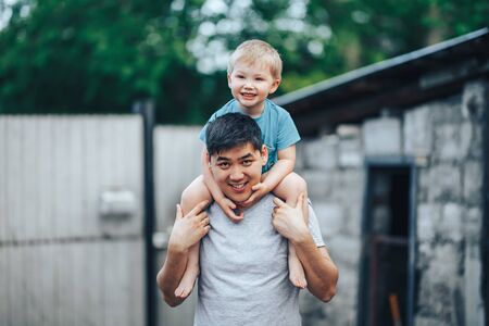 blonde three years old boy sitting on father's shoulders. Kazakh father and caucasian mother. Happy...