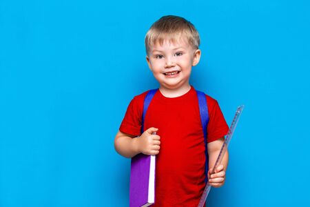 small happy smiling boy with glasses on his head, book in hands, schoolbag on his shoulders.の写真素材