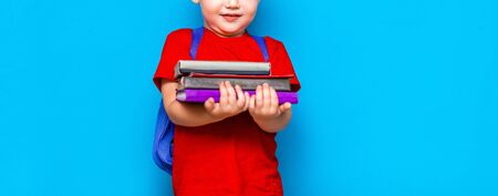 Smiling happy cute clever boy with backpack. Child with a pile of books in his hands. blue background. Ready for school. Back to school.の写真素材