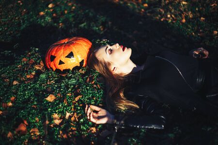 beautiful young blond woman with extravagant make-up in a black leather jacket with wide open eyes and an open mouth with a pumpkin in hands.の写真素材