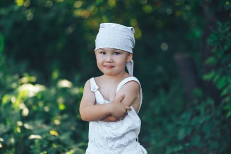 farmer kid with yellow squash in white casual clothes overalls and hat, standing in garden and smiling, harvest time.の写真素材