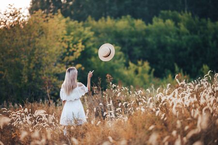 Rear view of blonde girl in autumn field in straw hat, dress. Back view of autumn portrait of woman outdoors.の写真素材