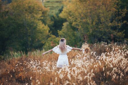 Rear view of blonde girl in autumn field in straw hat, dress. Back view of autumn portrait of woman outdoors.の写真素材