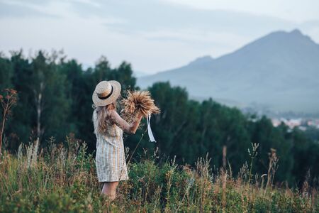 Rear view of blonde girl in autumn field in straw hat, dress. Back view of autumn portrait of woman outdoors.の写真素材