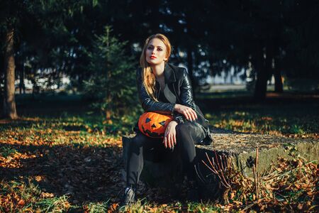 Beautiful modern witch holding halloween pumpkin in the forest. october. happy holidays.の写真素材