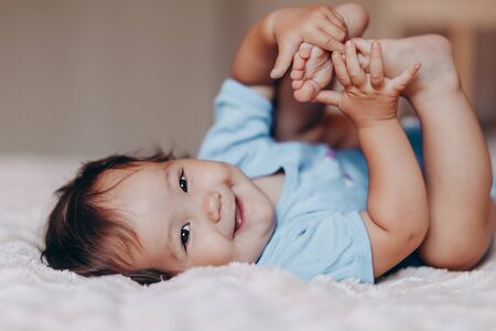 cute laughing one year old girl lying on bed and looking at camera touch her feet.の写真素材