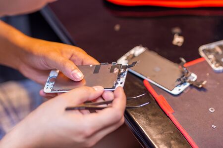 A man is repairing a mobile phone. In the frame, his hands and details of the device. repair shop for gadgets.の写真素材