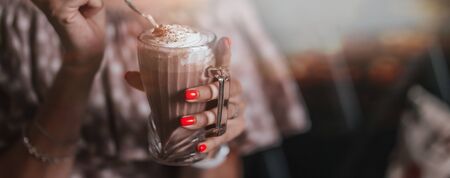 young woman sitting in cafe holding spoon ang glass with coffee or milkshake with whipped cream.の写真素材