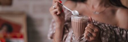 young woman sitting in cafe holding spoon ang glass with coffee or milkshake with whipped cream.の写真素材