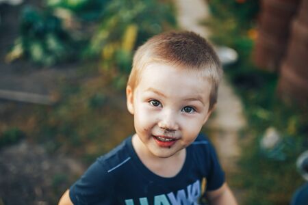 Blonde boy with disheveled hair smiling on a black couch after playing outside in the garden.の写真素材