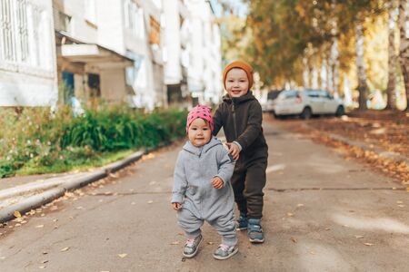 Cute 1 year old baby girl and 3 years old boy walking outdoors wearing in stylish overalls.の写真素材