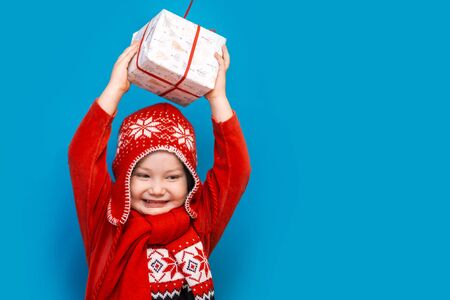 portrait of a happy little boy holding a new christmas gift with red ribbon in red clothes. happy new year, merry christmas.の写真素材