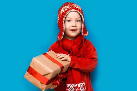 Christmas time. boy with Santa Claus Hat holding christmas gift with red tape and wery surprised face with open mouth.の写真素材