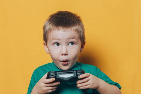 Little boy playing with black joystick have emotions on his face, he is surprisedon yellow...