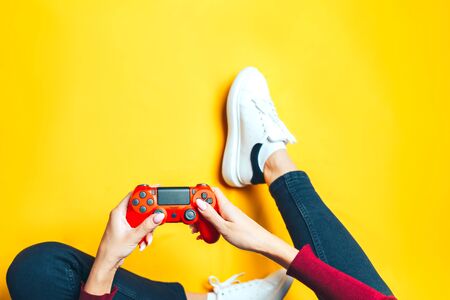 Young thin woman playing with red gamepad, sitting on yellow background. flat lay.の写真素材