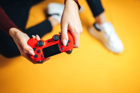 Young thin woman playing with red gamepad, sitting on yellow background. flat lay.の写真素材