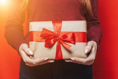Woman holding christmas gift with red ribbon in hands on red background.の写真素材