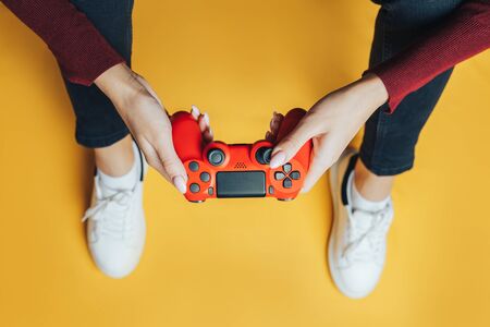 Young thin woman playing with red gamepad, sitting on yellow background. flat lay.の写真素材