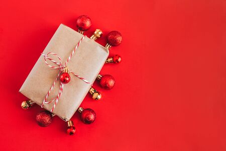 Christmas present in craft paper and red ribbon, small christmas ball on red bakground. Happy new year.の写真素材