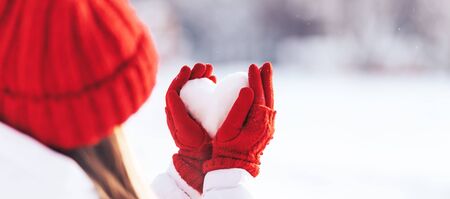 Woman in red gloves and hat holding heart shape from snow, Valentines day, sun set. love concept.