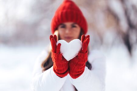 Woman in red gloves and hat holding heart shape from snowの写真素材