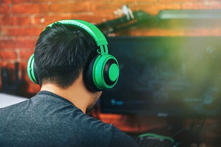 Back view of gamer in green professional headphones using computer for playing game.の写真素材