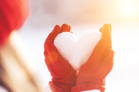 Woman in red gloves and hat holding heart shape from snow, Valentines day, sun set. love concept.の写真素材