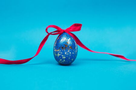 Close-up of blue painted Easter egg tied by red ribbon over blue background.の写真素材
