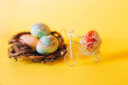 Colorful Easter eggs in the basket of white bicycle on yellow background. Bike hurry to Easter. Nest with eggs nearの写真素材
