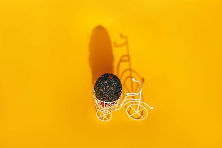 Vintage Easter egg on bike. Bicycle retro photo on yellow background with hard shadow.の写真素材