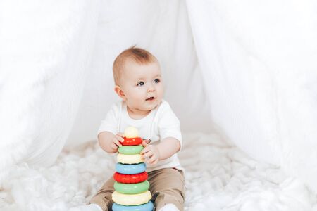 Little cute baby girl with a toy pyramid sitting in white interior at home.の写真素材