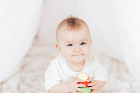 Little cute baby girl with a toy pyramid sitting in white interior at home.の写真素材
