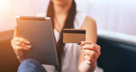 A young girl sits in chair with tablet and pays bills, online purchases, payment for goods during...