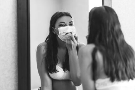 Young beautiful girl makes a make-up in medical maskの写真素材
