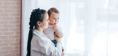 Sad mother sitting next to the window with babyの写真素材