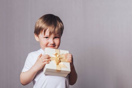 Beautiful little boy in a white T-shirt holding a gift in his handの写真素材