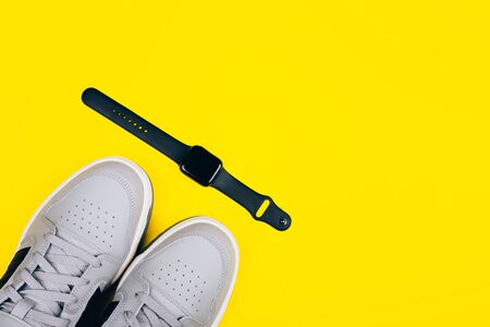 Stylish gray sneakers on a yellow background, stylish smart watches in black on a yellow background, healthy lifestyle, dietの写真素材