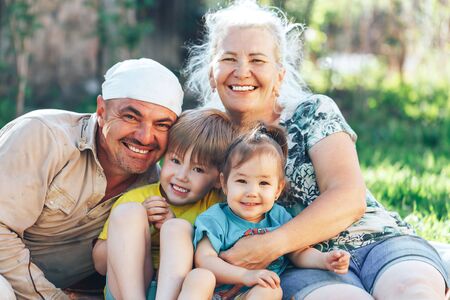 Happy family smiling grandfather grandmother with grandchildren sitting on open-air lawn on a sunny dayの写真素材