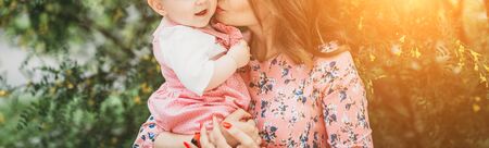 Young beautiful mother with small child in pink clothes on background of beautiful blooming tree in the open.の写真素材